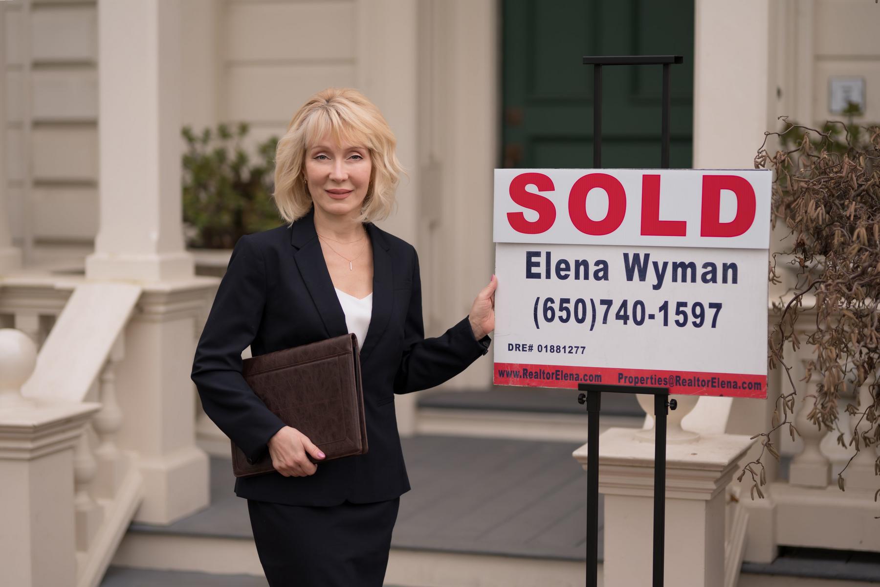 Elena Wyman next to a red SOLD sign in front of a sold home